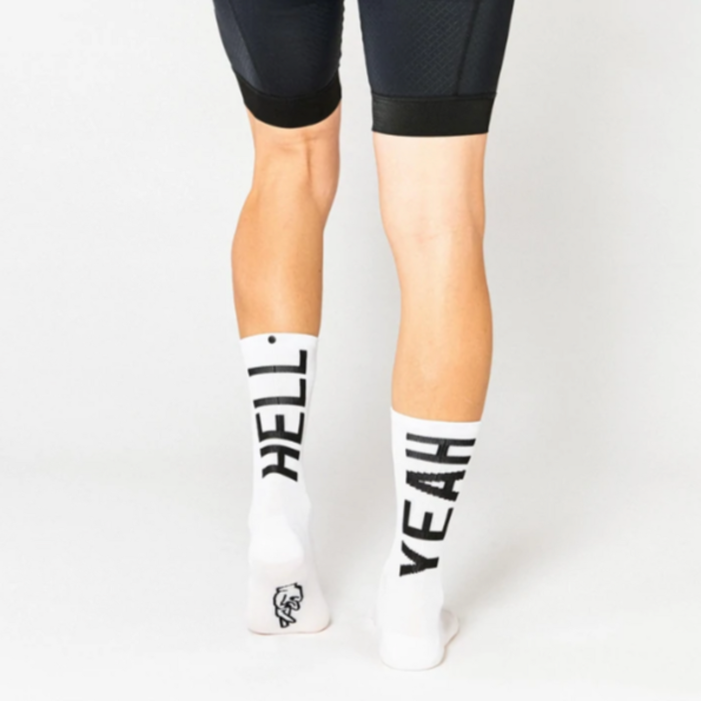 Cykelstrømpe i hvid med sort skrift både foran og bagpå "Hell yeah". Den er fra mærket Fingers crossed og modellen hedder #666 hell yeah 2.0.