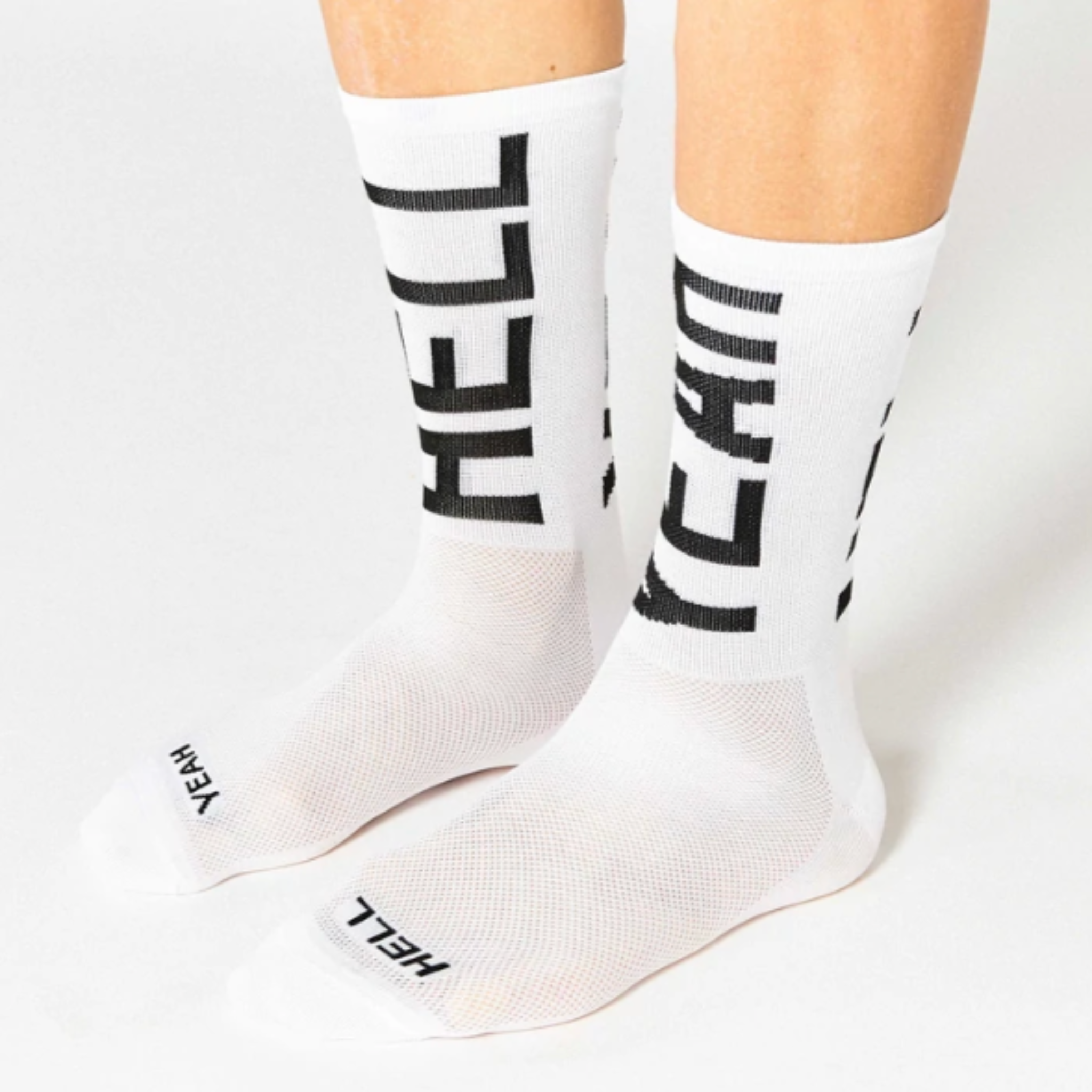 Cykelstrømpe i hvid med sort skrift både foran og bagpå "Hell yeah". Den er fra mærket Fingers crossed og modellen hedder #666 hell yeah 2.0.